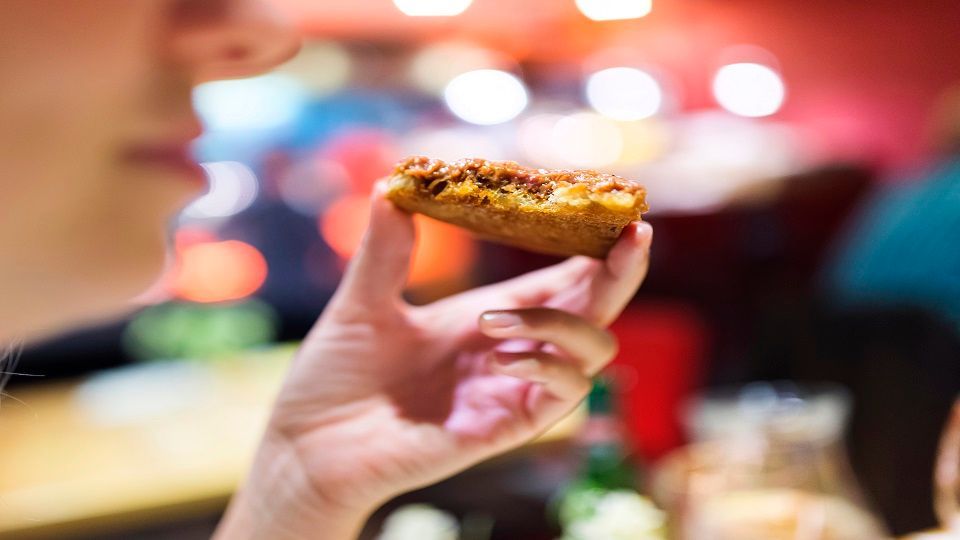 Unrecognizable young woman holding a piece of pizza and eating
