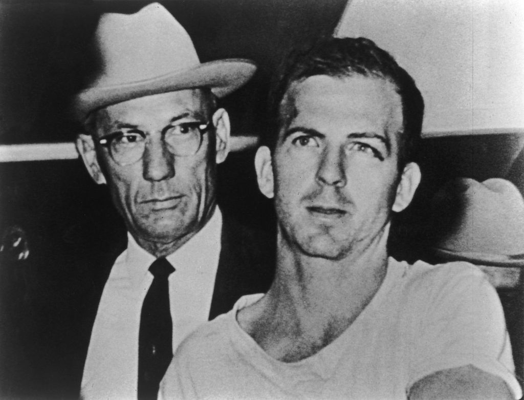 Lee Harvey Oswald (1939 - 1963) (R), alleged assassin of President John F. Kennedy, is detained by a police officer while under arrest, Dallas, Texas, November 1963. (Photo by Hulton Archive/Getty Images)
